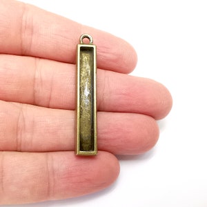 May include: A gold-toned metal pendant with a rectangular frame. The frame is open on the front and back, allowing for the insertion of a small object or image.