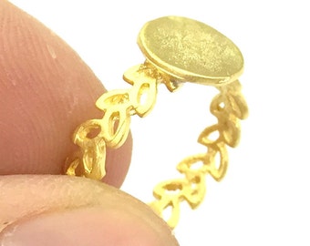 Op de afbeelding: Gouden ring met een ronde, lege, metalen bezel en een delicate, bladvormige band.