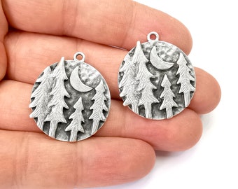 May include: Two silver charm pendants featuring a crescent moon and pine trees design. The pendants are round and have a textured finish.