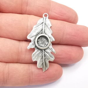 May include: Silver-toned metal pendant shaped like an oak leaf with a round, open space in the center for a cabochon.
