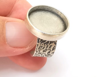 May include: Silver ring with a round, flat, silver bezel setting. The ring band has a textured design.