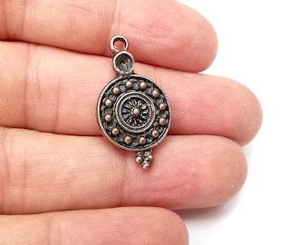 May include: A copper and silver charm with a circular design featuring a central flower motif surrounded by a ring of small beads.