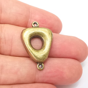 May include: A gold-toned metal pendant shaped like a triangle with a large, round hole in the center. The pendant has two loops at the top for attaching a chain or cord.