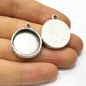 Könnte beinhalten: Zwei silberfarbene runde Anhänger-Tabletts mit abgeschrägter Kante. Die Tabletts sind für die Aufnahme eines runden Cabochons ausgelegt.