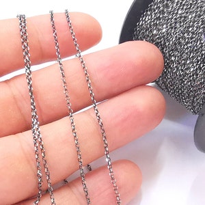 May include: Three strands of silver chain, each with a different length, are displayed on a hand. The chain is in a spool in the background.