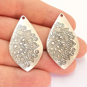 May include: Two silver teardrop-shaped metal charms with an intricate floral design.