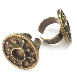 May include: Two antique gold adjustable rings with a circular design. The rings have a textured surface and a raised circular center.