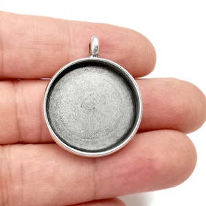 Op de afbeelding: Zilveren hangerbakje met een rond, glad, zilverkleurig oppervlak. Het bakje is ontworpen om een ronde cabochon te bevatten.