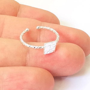 Puede incluir: Un anillo de plata con un diseño cuadrado texturizado. El anillo está hecho de una banda delgada con una textura de cuentas.