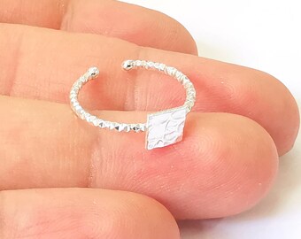May include: A silver ring with a textured square design. The ring is made of a thin band with a beaded texture.