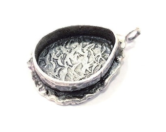 May include: Silver pendant with a detailed design on the back. The pendant is oval shaped and has a loop for attaching a chain.