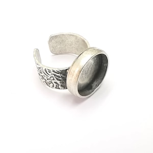 May include: A silver-toned adjustable ring with an oval bezel setting. The band features an etched floral design on one side and a smooth, open design on the other. The ring is set against a white background.