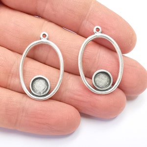 May include: Two silver oval-shaped pendant charms with a smaller circle in the center. The charms have a smooth, shiny finish.