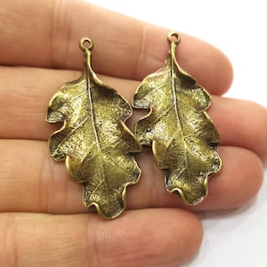 May include: Two antique gold-toned metal oak leaf charms with a detailed textured surface. The leaves have a hole at the top for hanging.