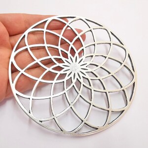 May include: Silver circular pendant with a geometric design of overlapping circles and lines, creating a flower-like pattern.