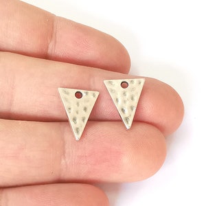 May include: Two silver triangle shaped metal charms with a hole in the top. The charms have a hammered texture.