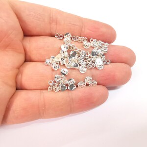 May include: A pile of silver earring backs, also known as earring clutches, in a hand. The earring backs are small and round with a loop on the back.