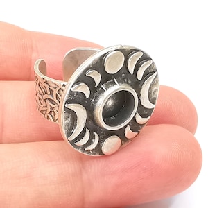 Op de afbeelding: Een zilveren ring met een ronde, getextureerde bovenkant met een maan- en sterrendesign. De band van de ring is ook getextureerd.