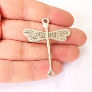 May include: Silver dragonfly charm with a detailed design and a loop at the bottom for attaching to jewelry or crafts.