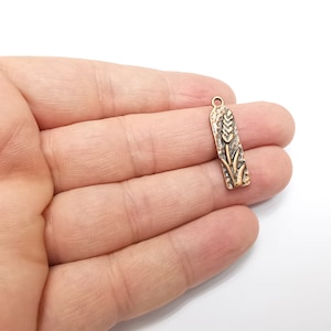 May include: Gold-toned metal charm with a wheat stalk design. The charm is in the shape of a rectangle with rounded edges.