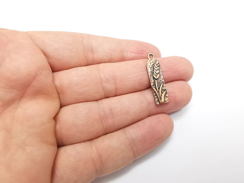 May include: Gold-toned metal charm with a wheat stalk design. The charm is in the shape of a rectangle with rounded edges.
