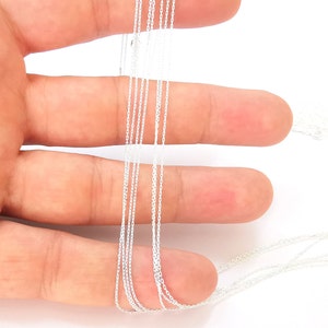 Può includere: Primo piano di una mano che tiene un fascio di catene d'argento. Le catene sono sottili e delicate, e sono tutte della stessa lunghezza. Le catene sono disposte in un mucchio ordinato, e sono tutte distese contro la mano.