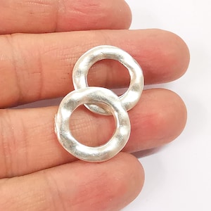 May include: Two silver-toned metal rings with a textured surface. The rings are interlocked and have a circular shape.