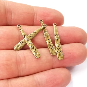 May include: Four gold-toned metal charms shaped like paddles with a geometric pattern. The charms have a loop at the top for attaching to jewellery or other crafts.