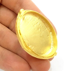 May include: A gold-coloured metal pendant with a round, smooth surface and a raised rim. The pendant has a slightly oval shape.