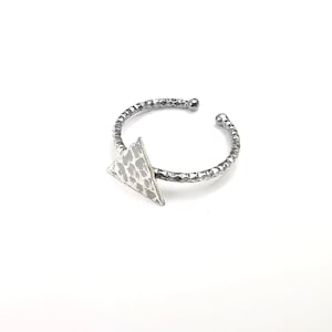 May include: A silver ring with a textured band and a triangular pendant. The pendant has a hammered finish and a geometric design.