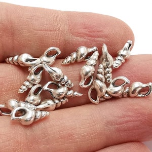 以下が含まれることがあります： それぞれ異なるデザインの銀色の貝殻チャームのグループ。チャームは小さく繊細で、ジュエリーやクラフトに遊び心を加えるのに最適です。