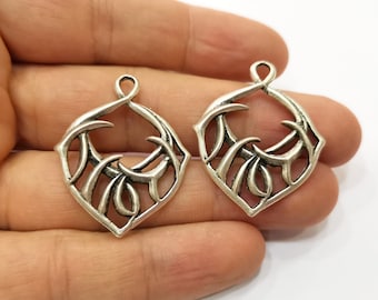 Op de afbeelding: Twee zilverkleurige metalen bedels in de vorm van een gestileerd blad met een open midden. De bedels hebben een delicaat, ingewikkeld ontwerp en zijn perfect voor het maken van sieraden.