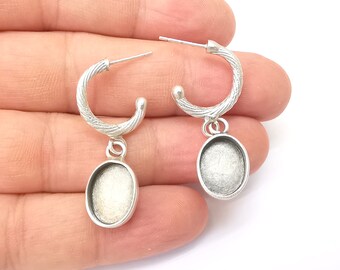 May include: A pair of silver hoop earrings with a textured design. Each hoop has a small oval-shaped pendant hanging from it.