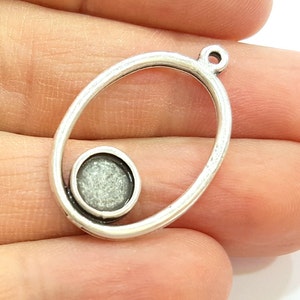 May include: Silver oval pendant with a round, open space in the center. The pendant has a loop at the top for attaching a chain.