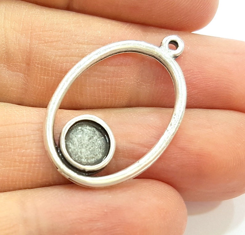 May include: Silver oval pendant with a round, open space in the center. The pendant has a loop at the top for attaching a chain.