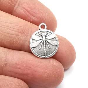 May include: Silver charm with a detailed dragonfly design. The dragonfly is centered on a round charm with a smooth surface.