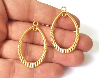 May include: Two gold-tone metal oval-shaped earring blanks with a textured design. The blanks have a jump ring at the top for attaching earring findings.