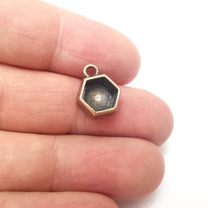 May include: A copper-toned hexagonal pendant with a clear glass insert. The pendant has a loop at the top for attaching to a chain or cord.
