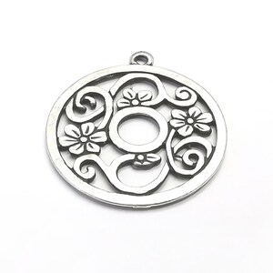 K&ouml;nnte beinhalten: Silberner Anh&auml;nger mit einem runden Design, das mit komplizierten Blumenmustern und einem zentralen offenen Kreis verziert ist. Der Anh&auml;nger hat oben eine Schlaufe zum Anbringen einer Kette.