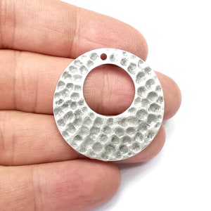 May include: A silver-toned metal circle pendant with a hammered texture and a hole at the top for hanging.