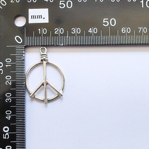 May include: Silver peace sign charm pendant measuring approximately 2 cm in diameter.