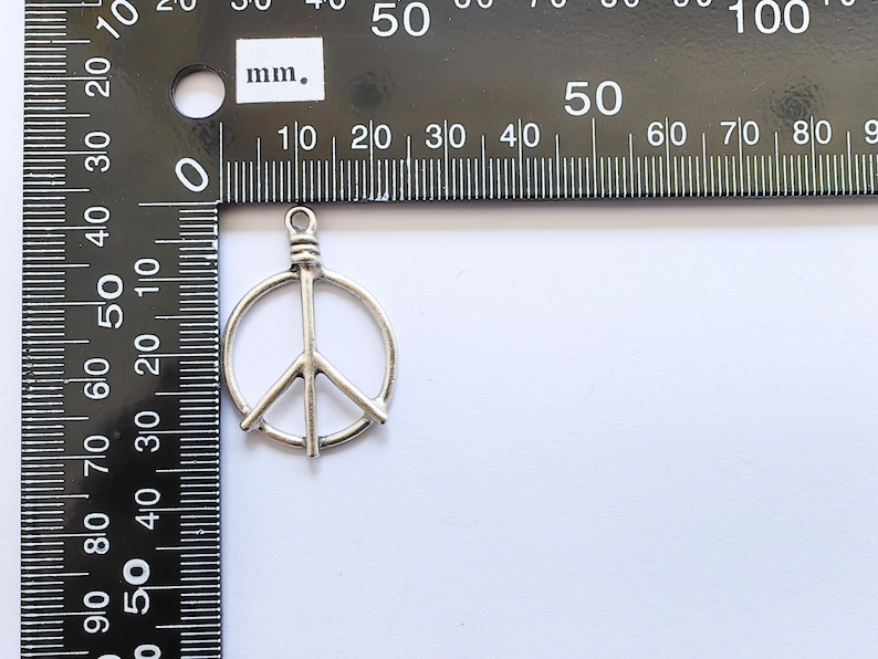 May include: Silver peace sign charm pendant measuring approximately 2 cm in diameter.