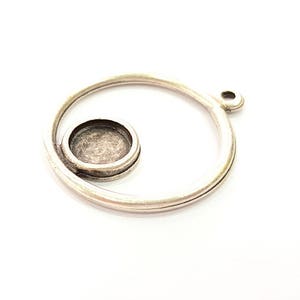 May include: A silver-coloured metal pendant with a spiral design. The pendant has a circular setting for a small stone or embellishment. The design includes a loop for attaching to a chain or cord.