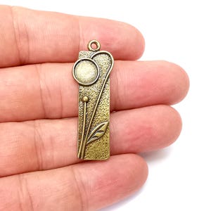 May include: A bronze pendant charm with a textured surface and a stylized floral design. The charm features a round circle with a raised center and a leaf with a stem.