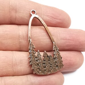 Könnte beinhalten: Ein kupferfarbener Metallanhänger in Tropfenform mit einem Ausschnitt in der Mitte. Der Anhänger zeigt ein detailliertes Design von fünf Kiefern mit strukturierten Nadeln.