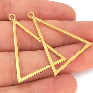 Puede incluir: Dos blanks para pendientes de forma triangular de color dorado. Los blanks están abiertos en la parte superior y tienen un bucle para sujetar una montura.