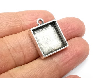 May include: Silver-toned square pendant with a clear glass insert. The pendant has a loop at the top for attaching to a chain or cord.