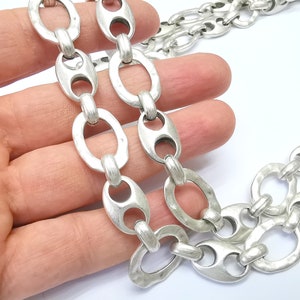 May include: Silver chain necklace with large oval links. The links have a textured, hammered finish.