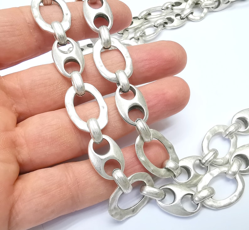 May include: Silver chain necklace with large oval links. The links have a textured, hammered finish.