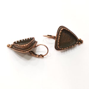 May include: A pair of copper triangle earring settings with a decorative border. The settings are designed to hold a cabochon stone.